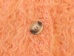 Gros plan du tissu tricoté orange duveteux avec un bouton marbré marron sur le gilet