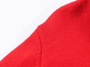 Close-up of red knit cardigan shoulder seam showing fine fabric texture and stitching