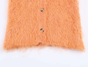 Gros plan sur un cardigan duveteux orange avec des boutons en corne et texture moelleuse