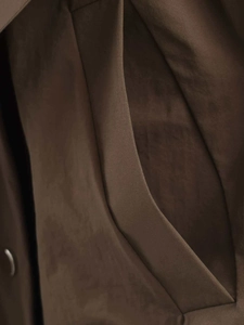 Detail of side pocket stitching and premium dark brown fabric on minimalist trench coat
