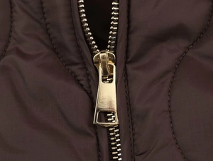 Détail du zip métallique doré sur une veste marron matelassée avec motif en losange