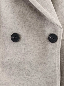 Detail of grey wool coat featuring wide lapel collar and symmetrical black buttons