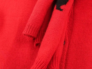 Detailed close-up of red knit cardigan fabric with black animal embroidery and button