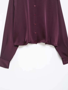 Detailed macro view of burgundy satin shirt featuring elastic hem and button closure