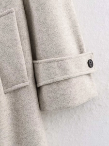 Detail of light gray wool coat sleeve featuring adjustable cuff strap and dark button