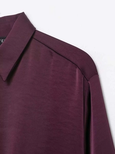 Detail of the smooth lapel and silky burgundy satin texture on the long-sleeve blouse