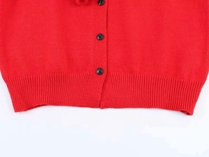 Detail of red knitted cardigan featuring black round buttons and ribbed hem texture