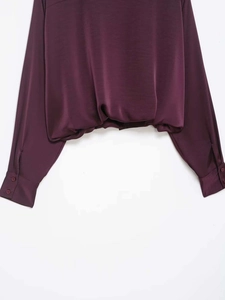 Detail view of burgundy satin shirt featuring ruched hem and buttoned cuffs design