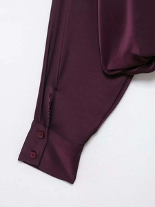 Detail of the burgundy satin shirt showing the double-button cuffs and smooth fabric texture