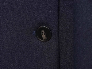 Detail view of navy blue wool fabric texture with a premium black round button on a coat