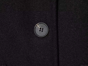 Close-up detail of a matte black round button and woven texture on a black wool coat