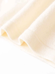 Macro shot of fine cream knit fabric texture with soft curled hem detail on top