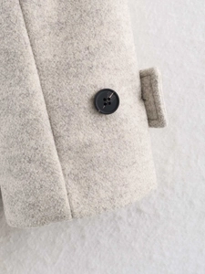 Detail of light gray wool coat sleeve with black button and precise stitching