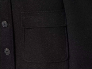Detail of a black wool coat featuring a large flap pocket and classic black buttons