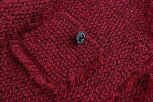 Macro d'une veste en tweed bordeaux avec poche à franges et bouton bijou vintage