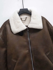 Detailed close-up of brown faux suede jacket with white faux fur lapels and metal zipper
