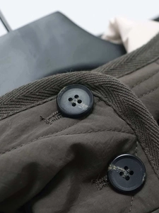 Dettaglio macro del tessuto del parka verde militare con bottoni neri e cuciture rinforzate