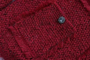 Gros plan sur la veste en tweed rouge avec fils métalliques et bouton fleur vintage
