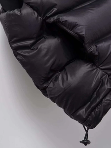 Detail of black puffer vest featuring smooth satin-like fabric and adjustable hem drawstring