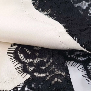 Macro shot of delicate black eyelash lace flower pattern on beige satin silk fabric