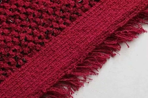 Détail du tissu en tweed rouge avec fils métalliques brillants et bordure à franges