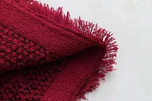Détail du tissu en tweed rouge avec fil métallique et bords frangés sur une veste