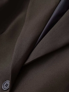 Detail view of a slim brown blazer showing smooth woven texture and matching button closure