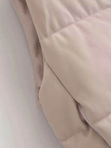 Detail view of the quilted faux leather puffer vest with precise side stitching in beige