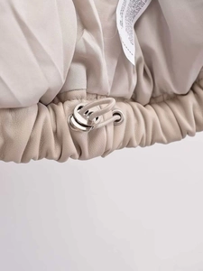 Detail of light beige faux leather vest hem featuring elastic drawstring and silver cord locks