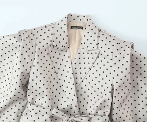 Détail du blazer à pois avec ceinture nouée et manches bouffantes sur fond blanc