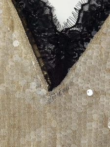 Close-up of golden sequin mesh fabric with black eyelash lace trim on V-neck dress