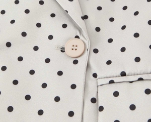 Détail macro du blazer à pois montrant la texture satinée et la fermeture à bouton mat