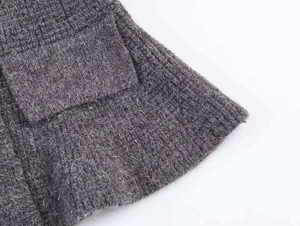 Close-up detail of grey thick knit cardigan texture with pocket flap and ribbed hemline
