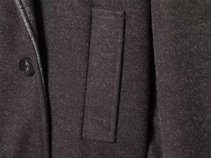 Detailed macro view of dark grey wool coat featuring a black button and side pocket