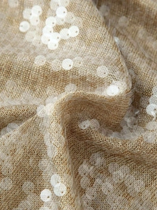 Close-up detail of champagne gold knit fabric with shimmering white translucent sequins