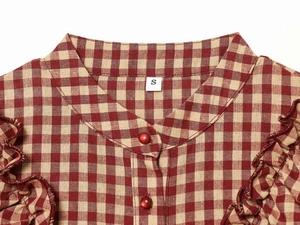 Detail of red and yellow plaid blouse featuring V-neckline with buttons and ruffled sleeves