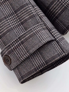 Close-up of vintage plaid blazer sleeve detail with brown button and fabric texture