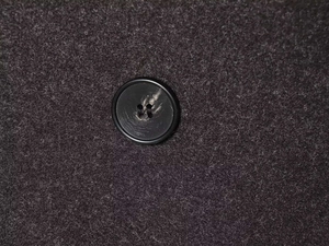 Macro shot of dark grey wool fabric texture and black round button on the coat detail