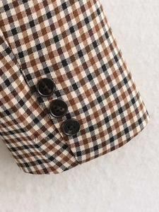 Dettaglio di tre bottoni neri sulla manica di un blazer in lana a quadri marroni