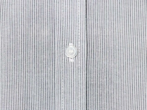 Close-up of fine vertical stripes fabric and a white button on a ruffle collar shirt