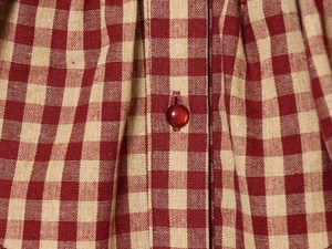 Detail of red gingham fabric texture and dark red button on a stylish layered shirt