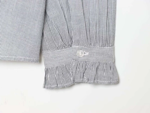 Detailed close-up of blue striped shirt cuff with ruffled edges and clear button