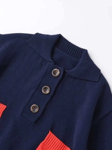 Detail view of navy knit cardigan featuring contrast orange pocket and brown textured buttons