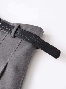 Detail of high waist grey trousers with a black crocodile texture belt and metal buckle