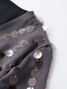 Detail of layered gold and brown sequins on a dark grey textured summer bodysuit
