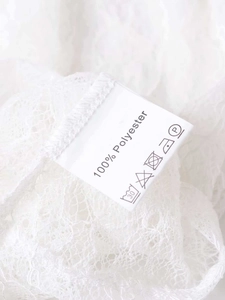 Détail de la dentelle blanche et étiquette d'entretien 100% polyester du haut