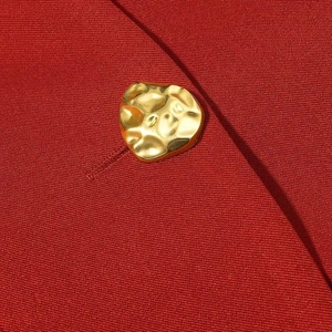 Detailed macro view of dark red twill blazer fabric and textured golden metal button