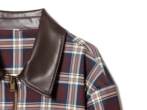 Détail de la veste à carreaux rouge et bleu avec col en similicuir marron et zip en bronze