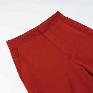 Detail view of the tailored waist with hidden closure and fine stitching on brick red trousers