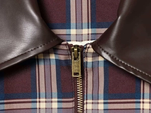 Gros plan d'une veste vintage à carreaux avec col en cuir marron et fermeture éclair